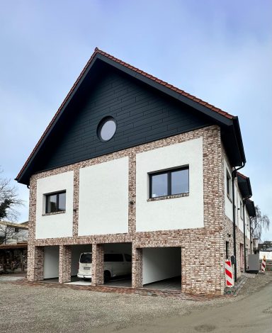 Modernes zweigeschossiges Gebäude mit rötlicher Steinfassade und Rundfenster.